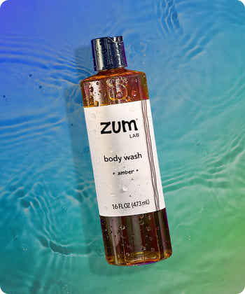 Amber scented bottle of body wash flying in the air with water droplets on it. Watery Blue to green gradient background.