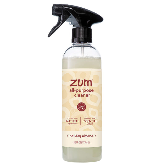 A 16 fl oz trigger spray bottle of Zum All-Purpose Cleaner in the holiday almond scent. The clear bottle shows a light beige liquid inside, featuring a cream-colored label with brown text and a black spray trigger on a solid white background.