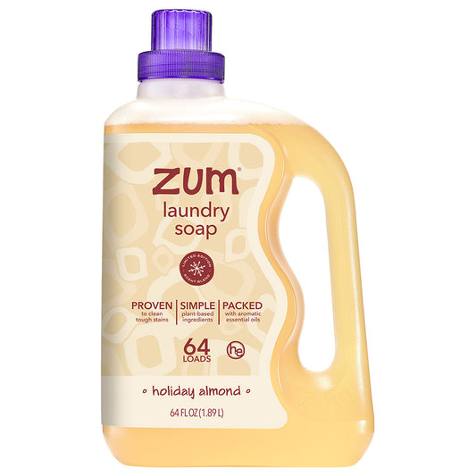 A 64 fl oz bottle of Zum Laundry Soap in the Holiday Almond scent, featuring a translucent yellow-amber liquid, a cream-colored label with brown text, and a purple cap, set against a plain white background.