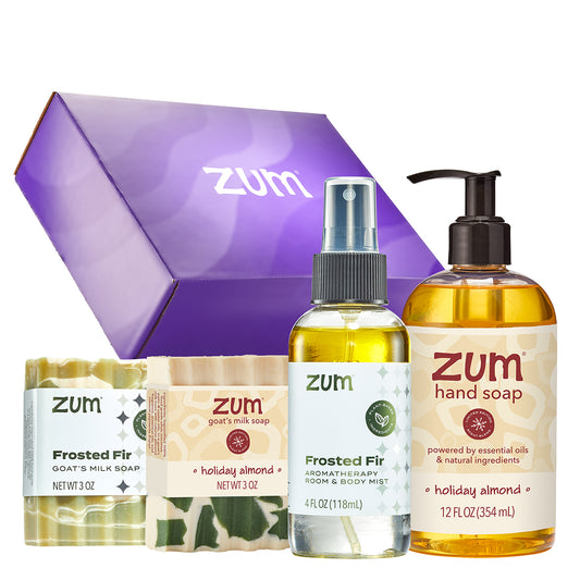A Zum gift set featuring a purple gift box, a frosted fir goat milk soap bar, a holiday almond aromatherapy room and body mist, and a hand soap bottle, all arranged on a white background.