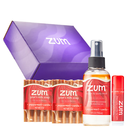 Zum body care gift set featuring a purple gift box, a bottle of peppermint-vanilla body mist, goat's milk soaps, and a Zumbo lip balm tube on a white background.