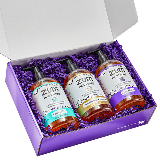 Rectangular gift box with a lid containing 3 hand soaps with purple crinkle packing material.