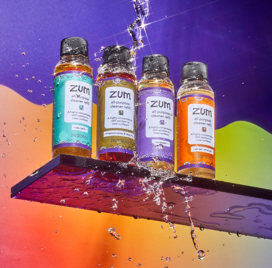 Four All Purpose Cleaner refill bottles lined up on purple shelf with water pouring over them.