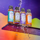 Four All Purpose Cleaner refill bottles lined up on purple shelf with water pouring over them.
