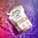 Pouch filled with Frankincense & Myrrh scented hand soap laying on a watery surface. Pink to purple gradient background.