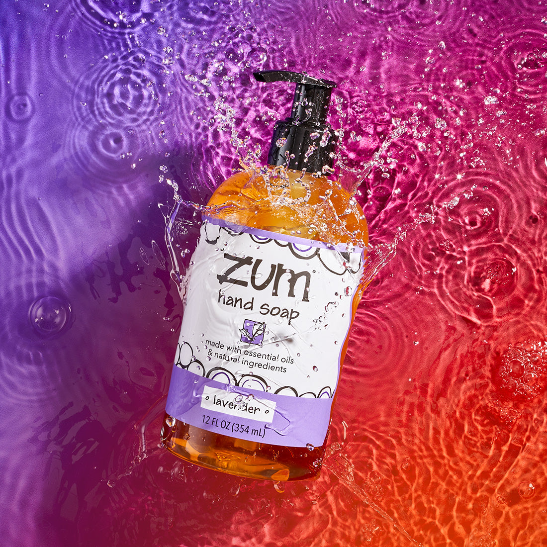 Lavender scented hand soap in a bottle with a pump, falling onto a watered surface with splashing. Purple to orange gradient background.