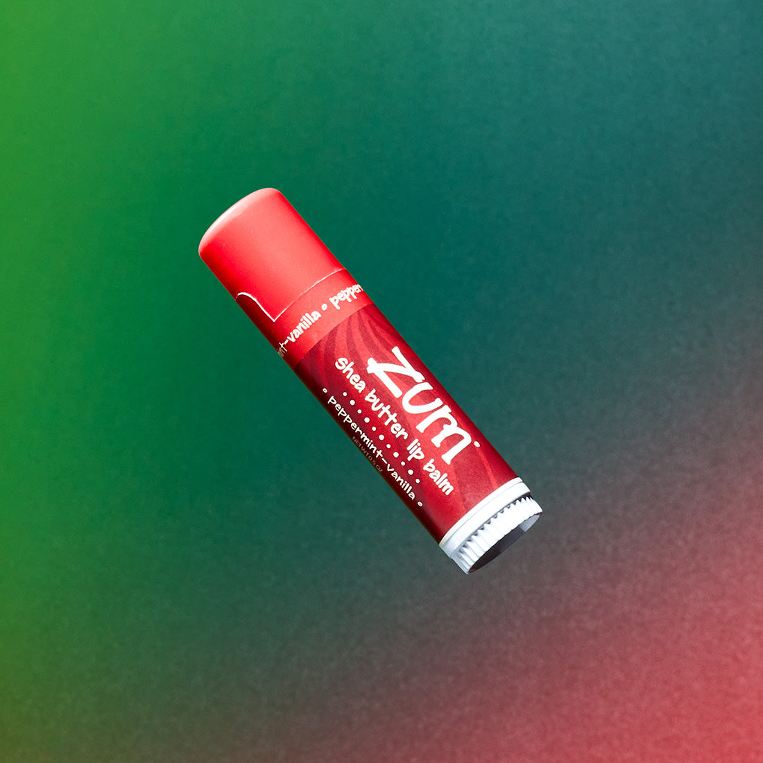 0.5 tube of lip balm in the flavor peppermint-vanilla flying in the air with a green to red gradient background.