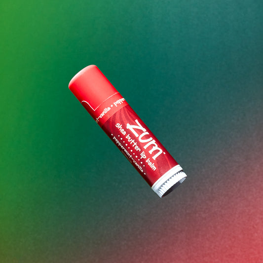 0.5 tube of lip balm in the flavor peppermint-vanilla flying in the air with a green to red gradient background.