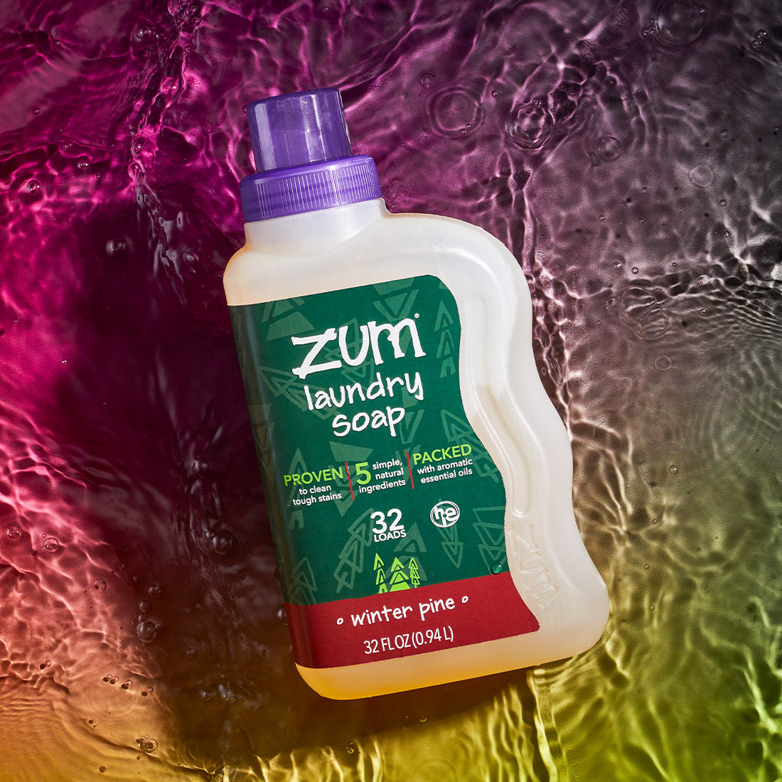 Winter Pine scented 32 fl. oz. bottle of laundry soap laying on a watered surface with a pinkish red to green gradient background.