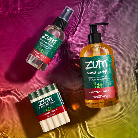 Winter Pine scented mist bottle, bar soap, and hand soap bottle laying on a watered surface with a pinkish red to green gradient background.