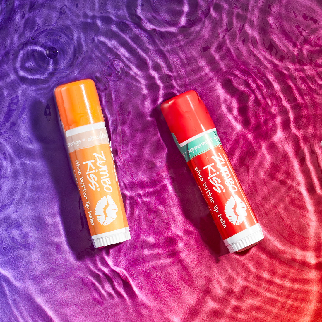 Almond-Orange and Peppermint flavored zumbo kiss tubes laying on a watered surface. purple to pinkish red gradient background.