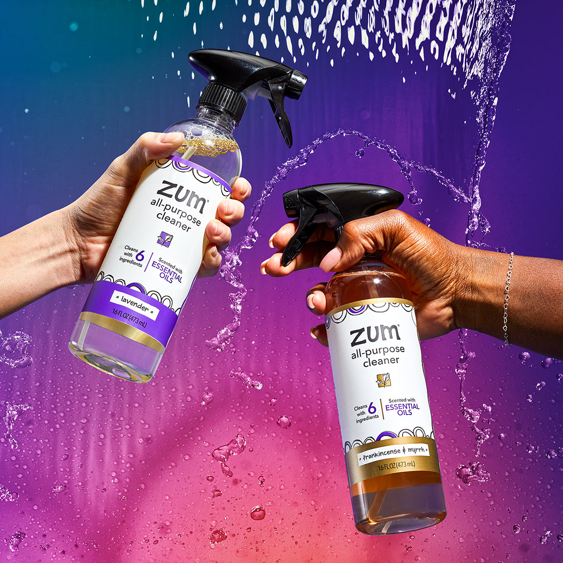 Two hands coming from the left and the right, holding a Lavender and Frankincense & Myrrh All-Purpose Cleaner bottles respectively. Water cascading in the back with a blue to purple to pink gradient background.