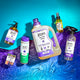 An assortment of product laying partially on a blue wave on the top half and blue/purple gradient water below. From left to right, top to bottom: Lavender Hand Soap, Geranium-Patchouli Bar Soap, Lavender Min Body Soap, Lavender 64 fl oz Laundry Soap, Lavender-Lemon Mist, and Lavender All-Purpose Cleaner.