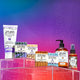 Assorted products on acrylic boxes with a blue, pink, and purple gradient background. Products from left to right: Lavender Hand & Body Lotion; Lavender-Mint, Patchouli, Frankincense & Myrrh, and Sea Salt Bar Soaps; Amber Hand soap; and Frankincense & Myrrh Mist.