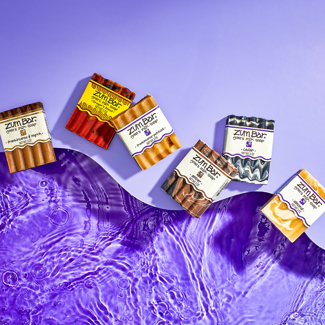 Frankincense & Myrrh, Dragon's Blood, Frankincense-Patchouli, Amber, Cedar, and Almond Bar Soaps laying at the edge of a light purple wave, on top of purple water.