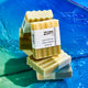 Two stacked Lemon-Rosemary bars, with a labeled version on top leaning agains a mirror. Water at the bottom, with a green to blue gradient colored background.