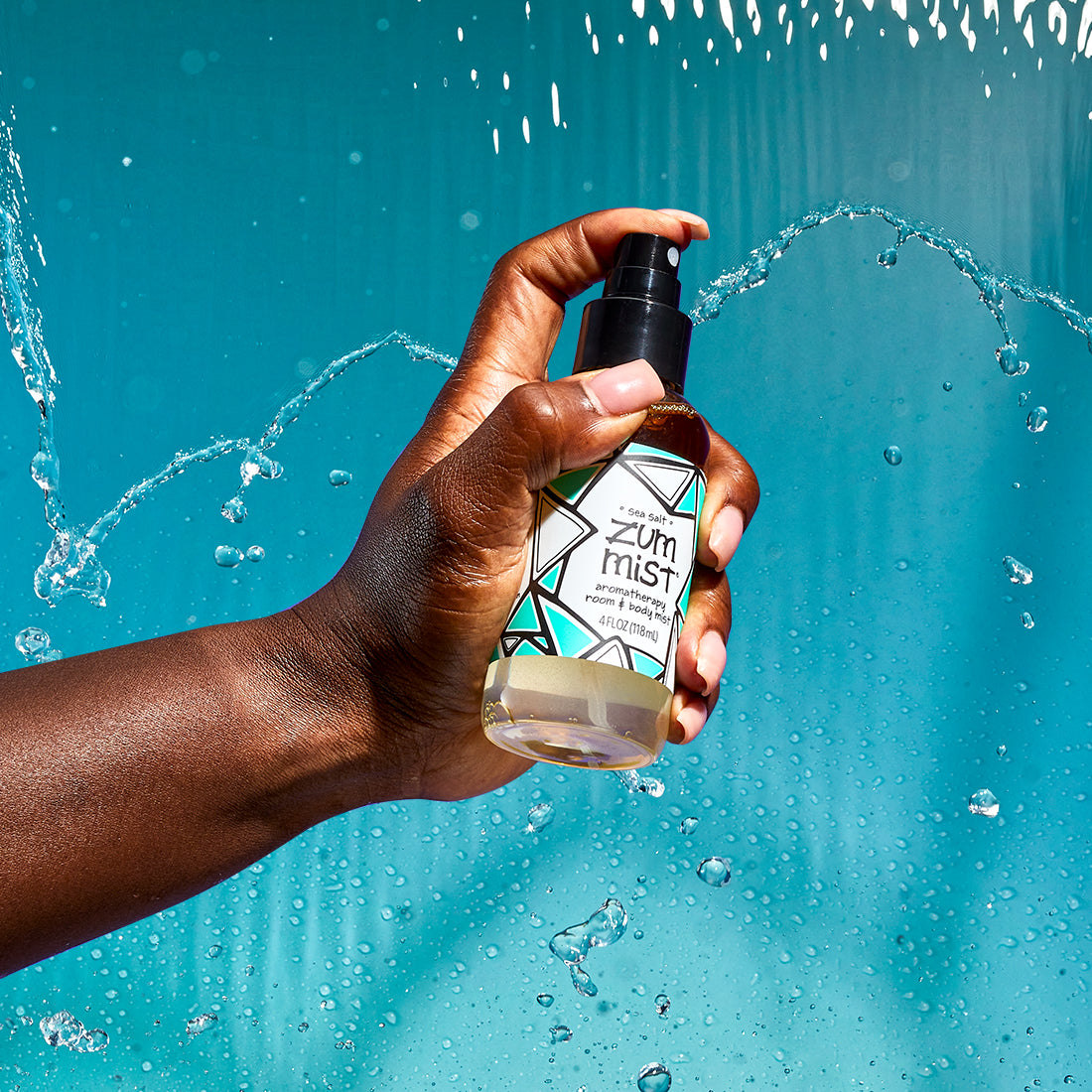 A hand coming from the left spraying a Sea Salt mist. Water falling behind it and a brown background.