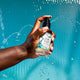 A hand coming from the left spraying a Sea Salt mist. Water falling behind it and a brown background.