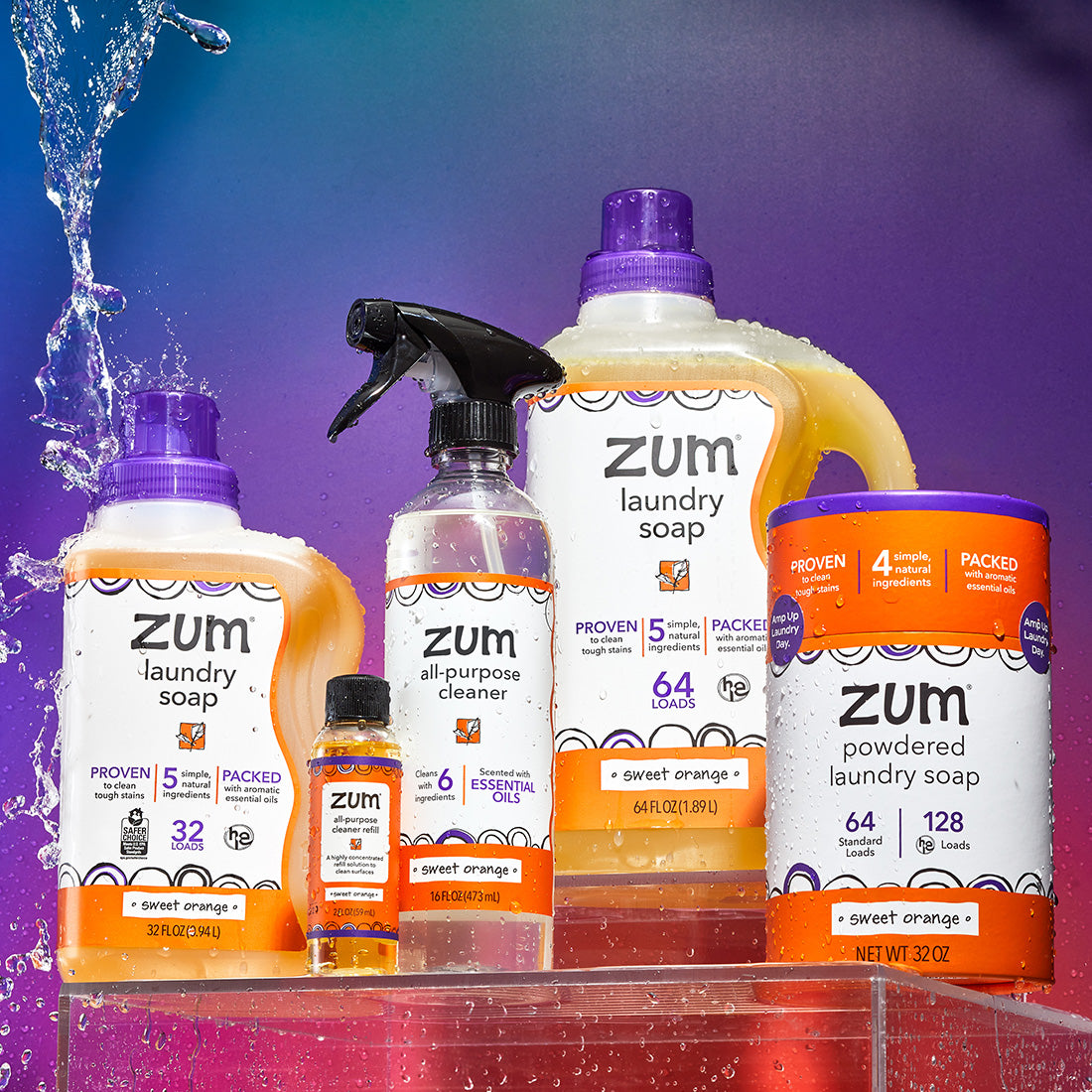 Sweet Orange home products on a clear acrylic box with water falling behind and on the product and a blue, orange, and purple gradient background. From left to right: 32 fl oz Laundry Soap, All-Purpose Cleaner refill, All-Purpose Cleaner, 64 fl oz Laundry Soap, and Powdered Laundry Soap.
