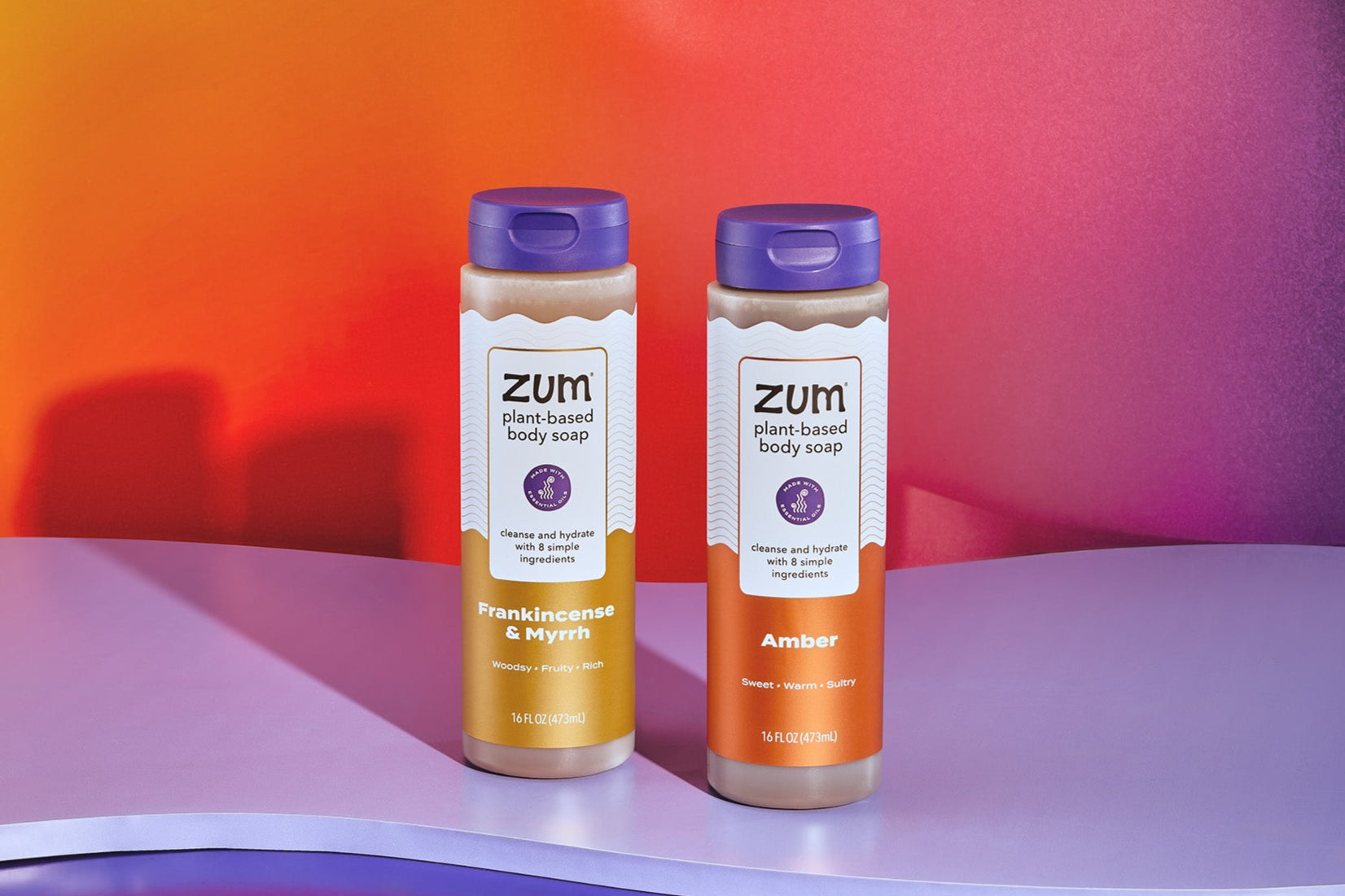 Frankincense & Myrrh and Amber Body Soap bottles on a light purple wave shape and a orange to pink gradient background.