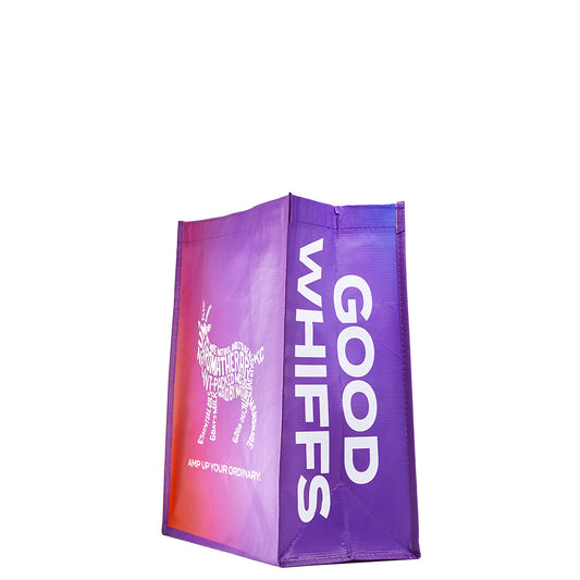 Side angle of recyclable tote bag. Good Whiffs phrase on the front, and goat and 'amp up your ordinary' slogan on the side of the bag. Orange to purple gradient color on the bag.