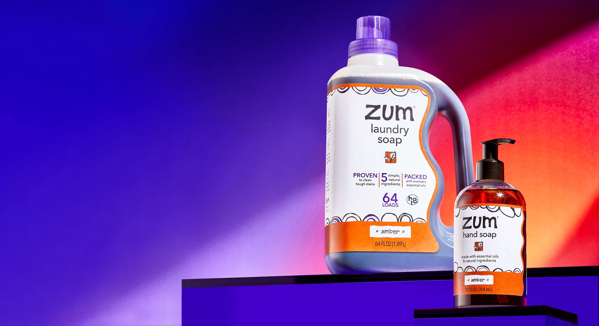 Amber scented 64 fl. oz. Laundry Soap battle and Hand Soap bottle with a pump on purple risers. Blue to purple to orange gradient background.