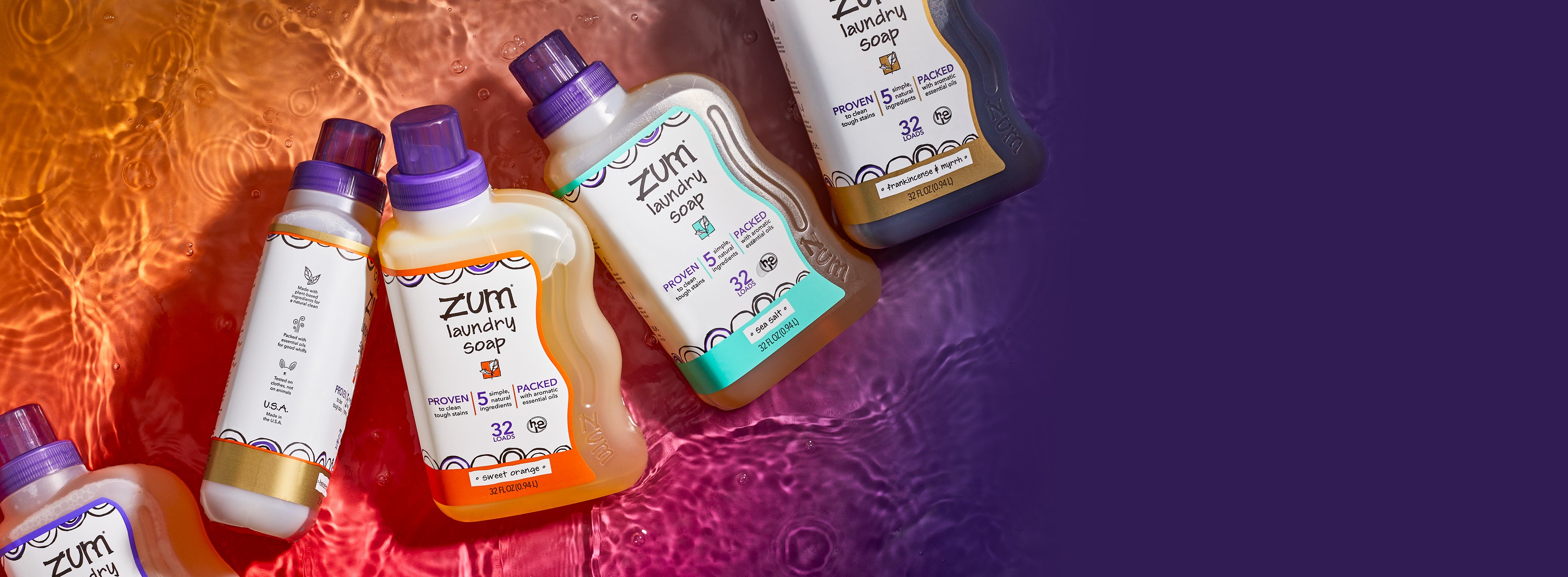 5 bottles of laundry soap in the scents Lavender, Frankincense-Patchouli, Sweet Orange, Sea Salt, and Frankincense & Myrrh laying on water. Orange to purple gradient background.