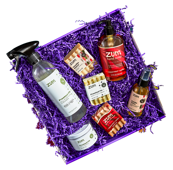 Open purple box gift filled with purple crinkle. The gift consists of a Frosted Fir All-Purpose Cleaner, Soy Candle, and Bar Soap; a Vanilla Spice Bar Soap and Room & Body Mist; and a Peppermint-Vanilla Bar Soap and Hand Soap. 