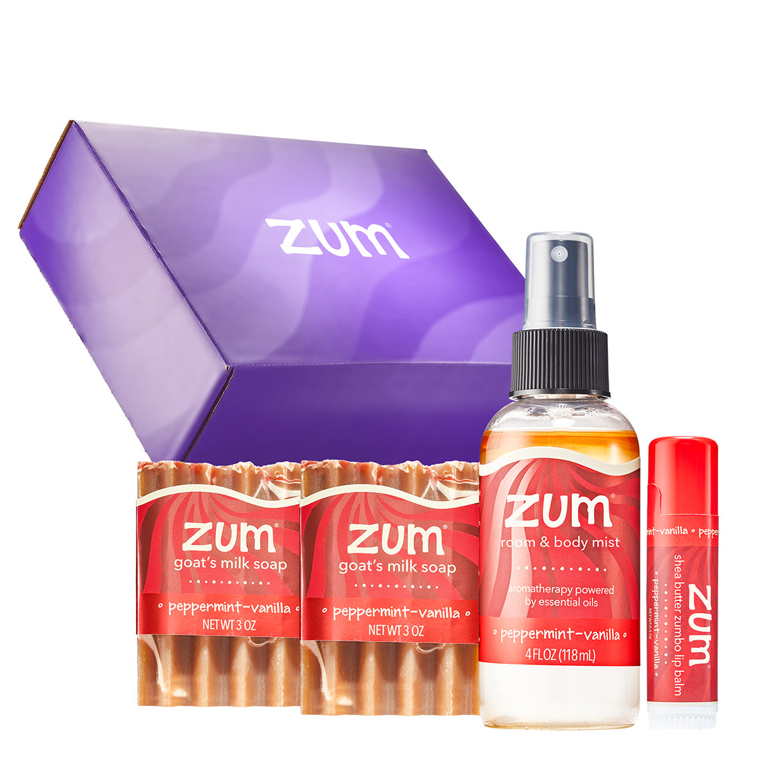 Zum body care gift set featuring a purple gift box, a bottle of peppermint-vanilla body mist, goat's milk soaps, and a Zumbo lip balm tube on a white background.