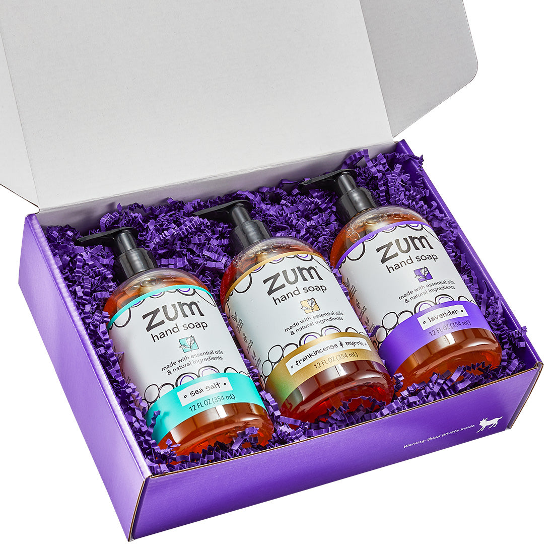 Rectangular gift box with a lid containing 3 hand soaps  with purple crinkle packing material.
