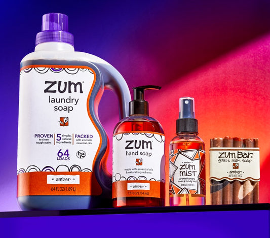 Amber Laundry Soap, Hand Soap, Room Mist, and Bar Soap all in a line next to each other on a purple platform.