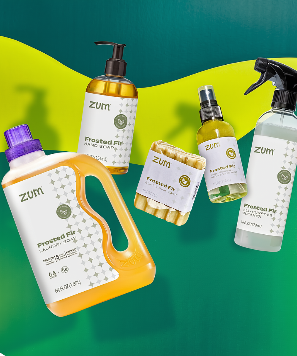 A set of Zum Frosted Fir products on a green and yellow graphic background: a laundry soap, hand soap, bar soap, room & body spray, and an all-purpose cleaner.