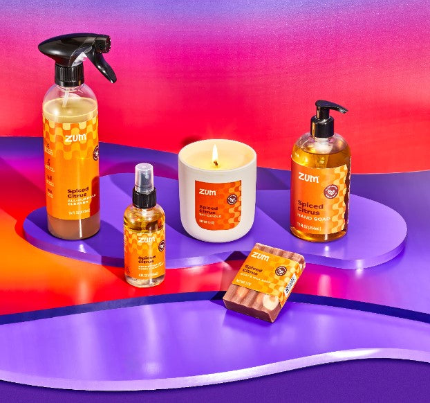 Spiced Citrus all-purpose cleaner, room mist, soy candle, bar soap, and hand soap on a purple table.