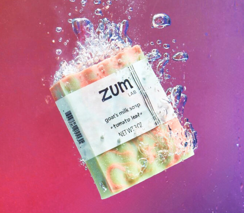Bar of soap with 'zum lab' label surrounded by water droplets on a gradient background
