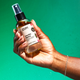 Hand holding Vanilla Spice Mist on green background.