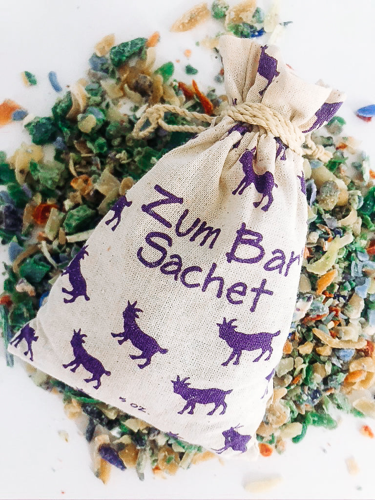 Muslin bag with purple goats filled with soap shavings laying on top of soap shavings